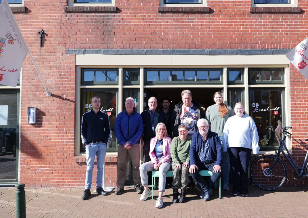 Wethouder Pieter Braaksma zit rechts vooraan in een groep van elf personen voor een rood bakstenen gebouw
